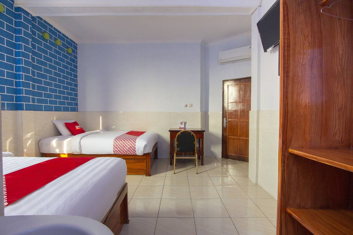 Une chambre d’hôtel avec deux lits, une petite table, une chaise, une armoire en bois et un téléviseur fixé au mur.