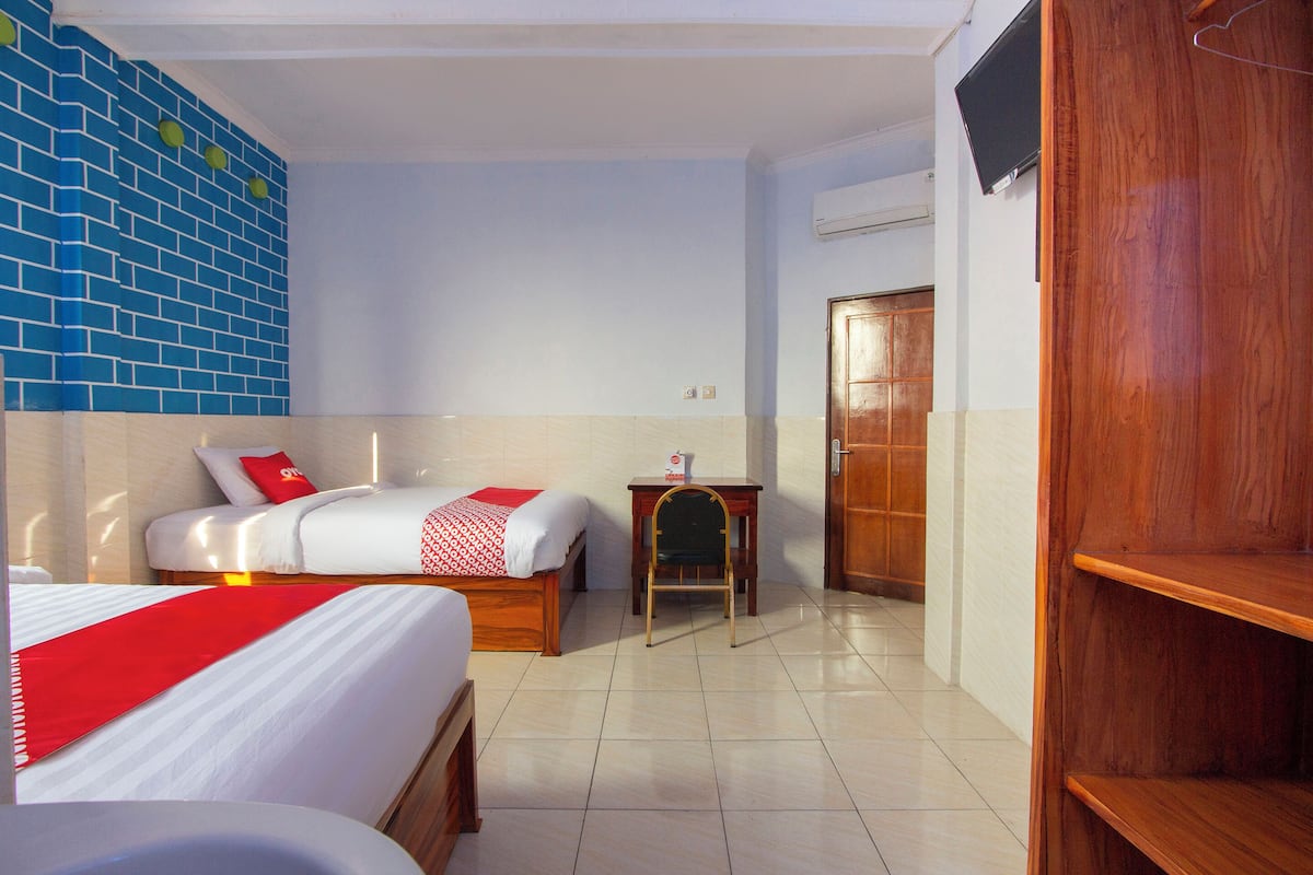 A hotel room with two beds, a small table, a chair, a wooden wardrobe, and a television on the wall.