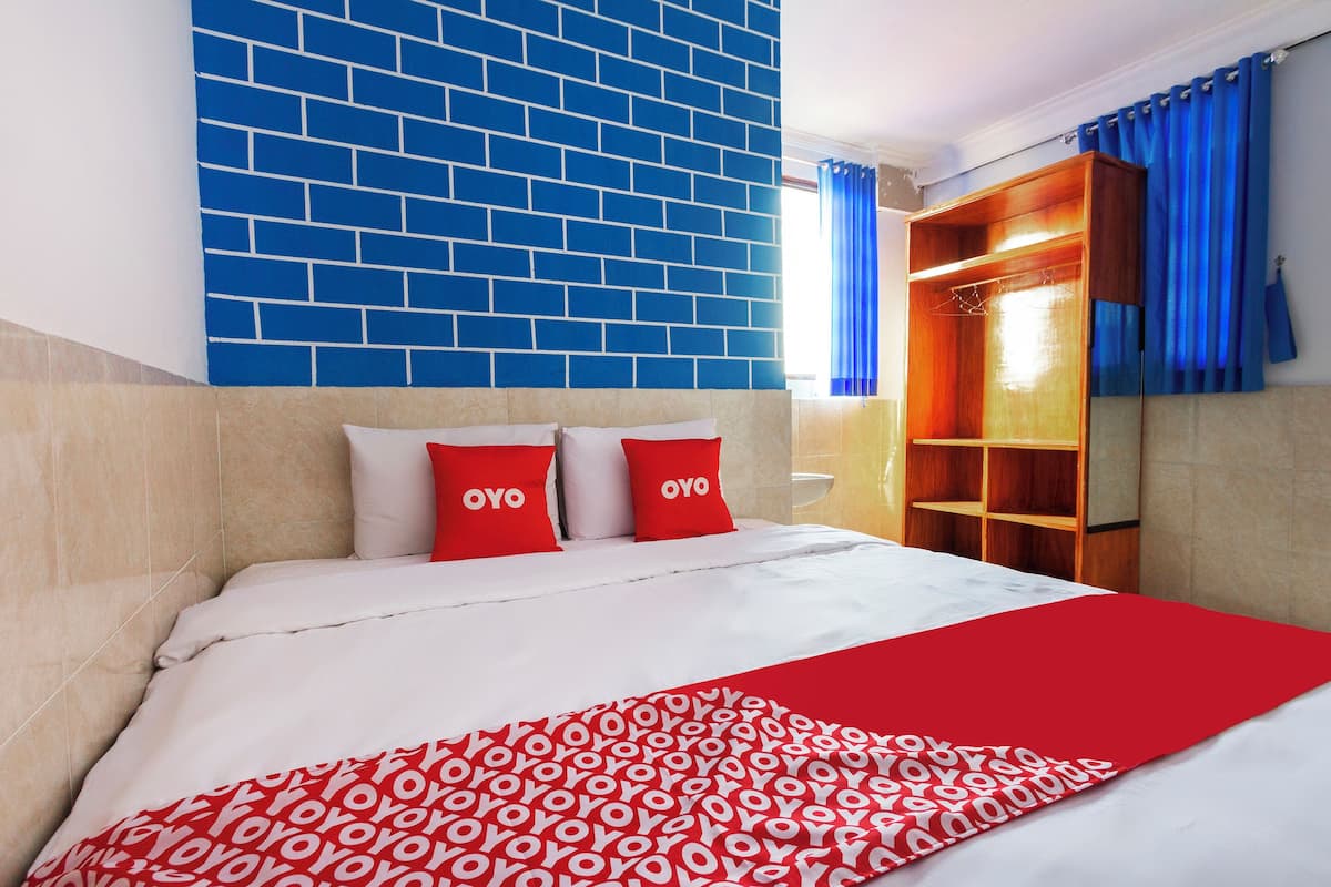 A bed with a white and red patterned bedspread, two pillows with 'OYO' text, a blue brick wall, and a wooden wardrobe with blue curtains.