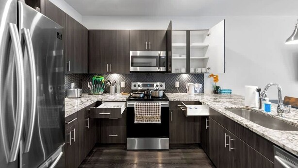 A modern kitchen with dark wood cabinets, stainless steel appliances, a granite countertop, and a built-in oven. - Apt 335 · Luxury 2Bd Queen Unit | Free Parking |Hwy121| TPC (McKinney)