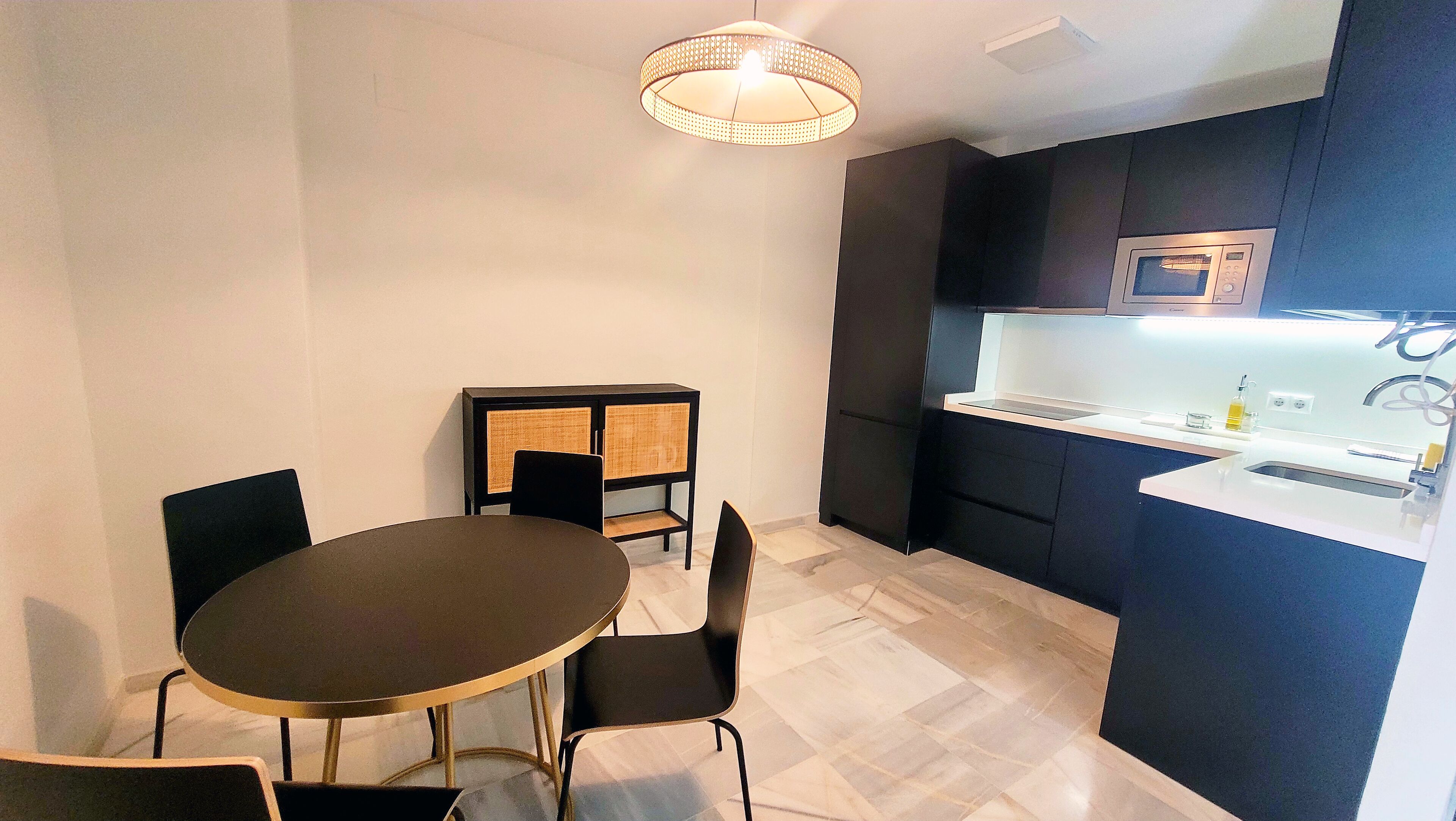 Una cocina compacta equipada con microondas, un lavamanos y una zona de comedor con mesa y sillas.