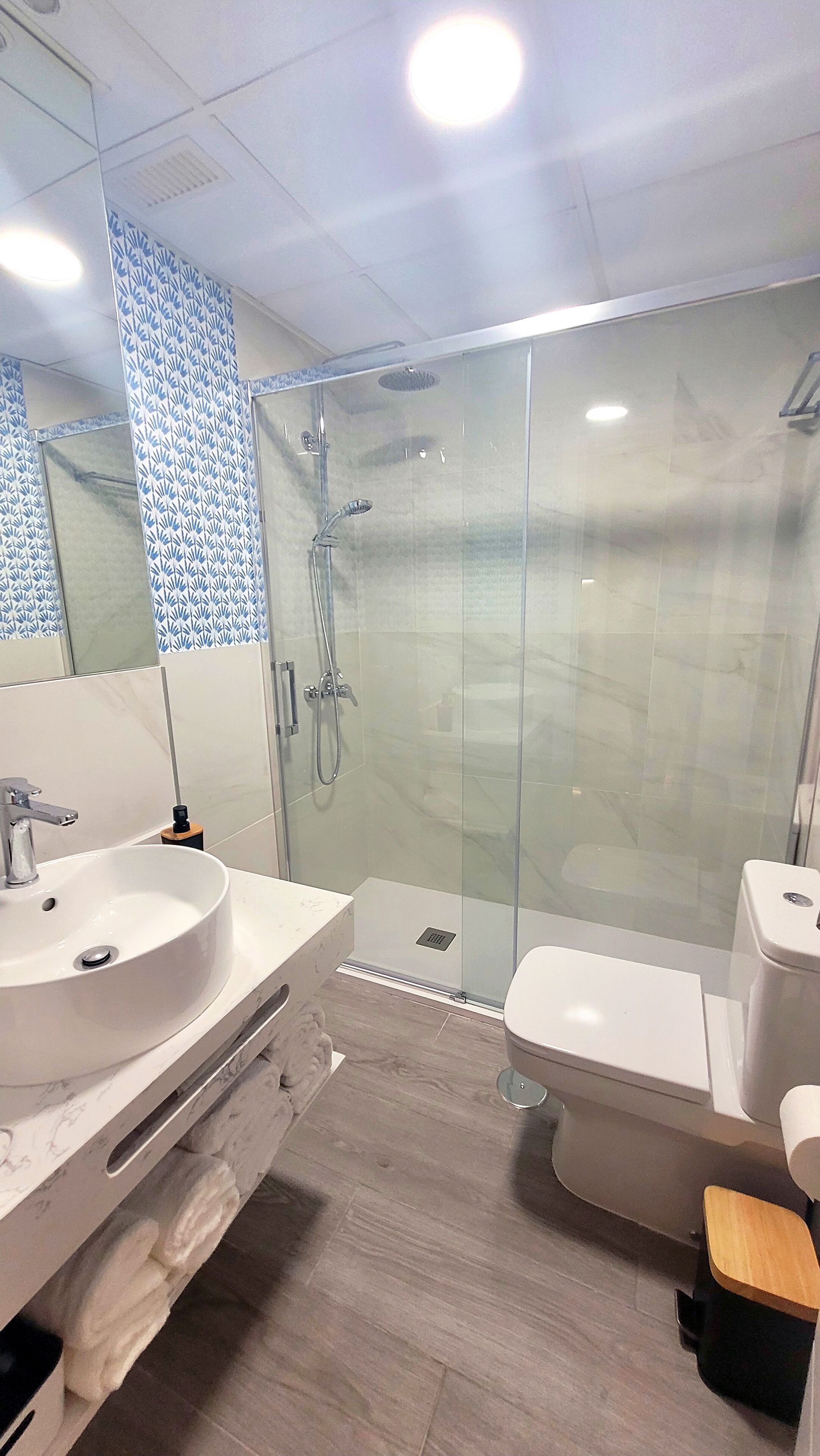 Un baño moderno con ducha de vidrio, un lavabo blanco y un inodoro.