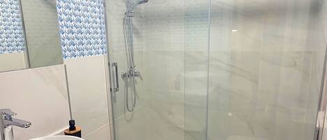 Un baño moderno con ducha de vidrio, un lavabo blanco y un inodoro.