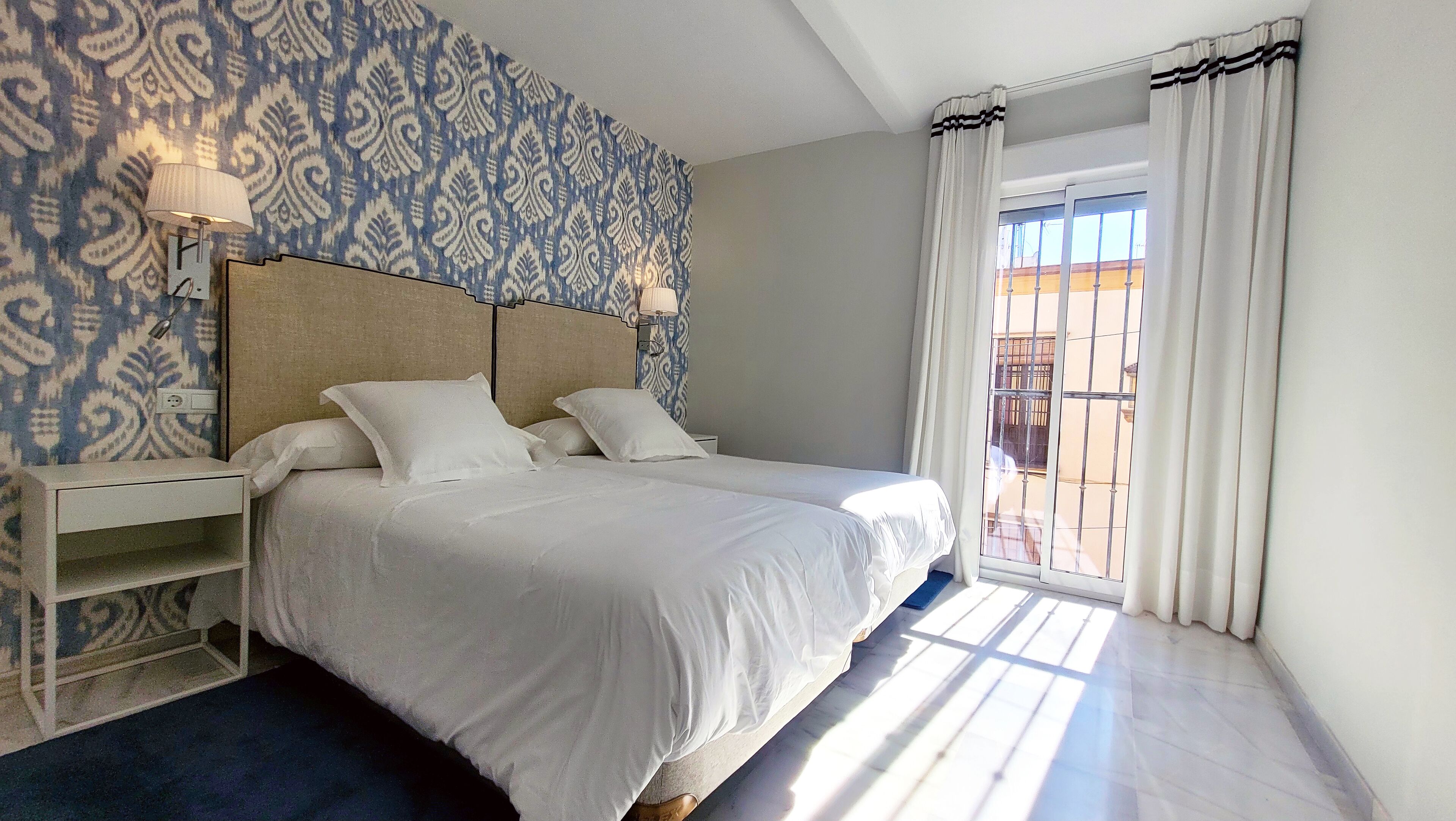 Habitación de hotel con una cama grande, una mesita de noche, una lámpara y un papel tapiz estampado.
