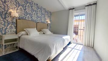 Habitación de hotel con una cama grande, una mesita de noche, una lámpara y un papel tapiz estampado.