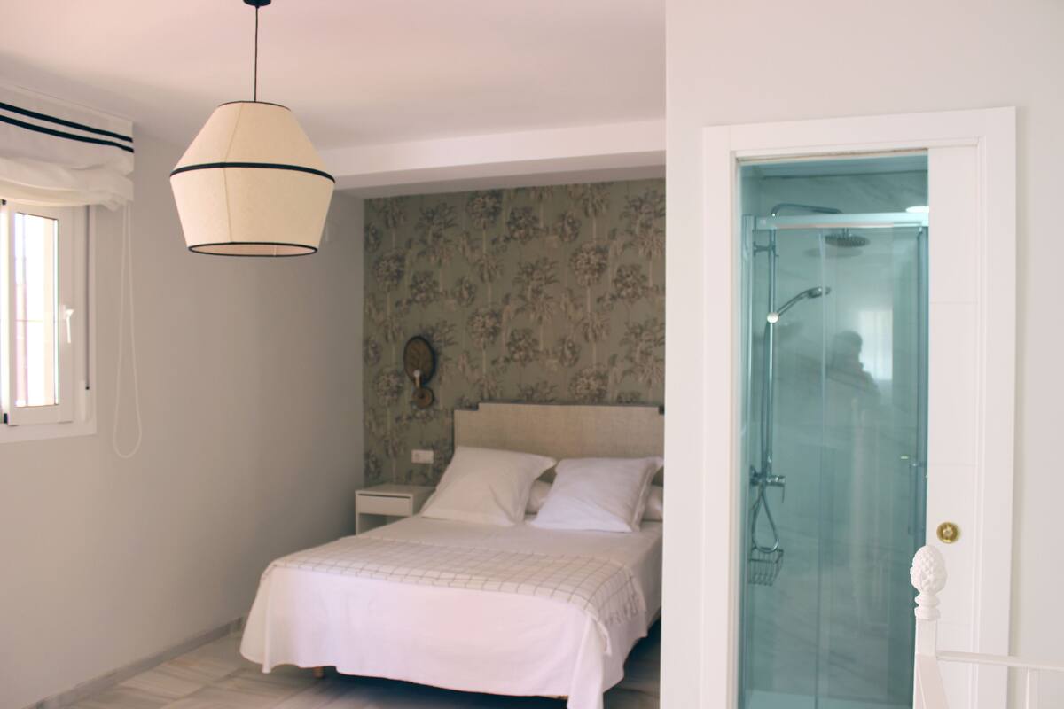 A bedroom with a bed, a nightstand, a wall clock, and a shower door.