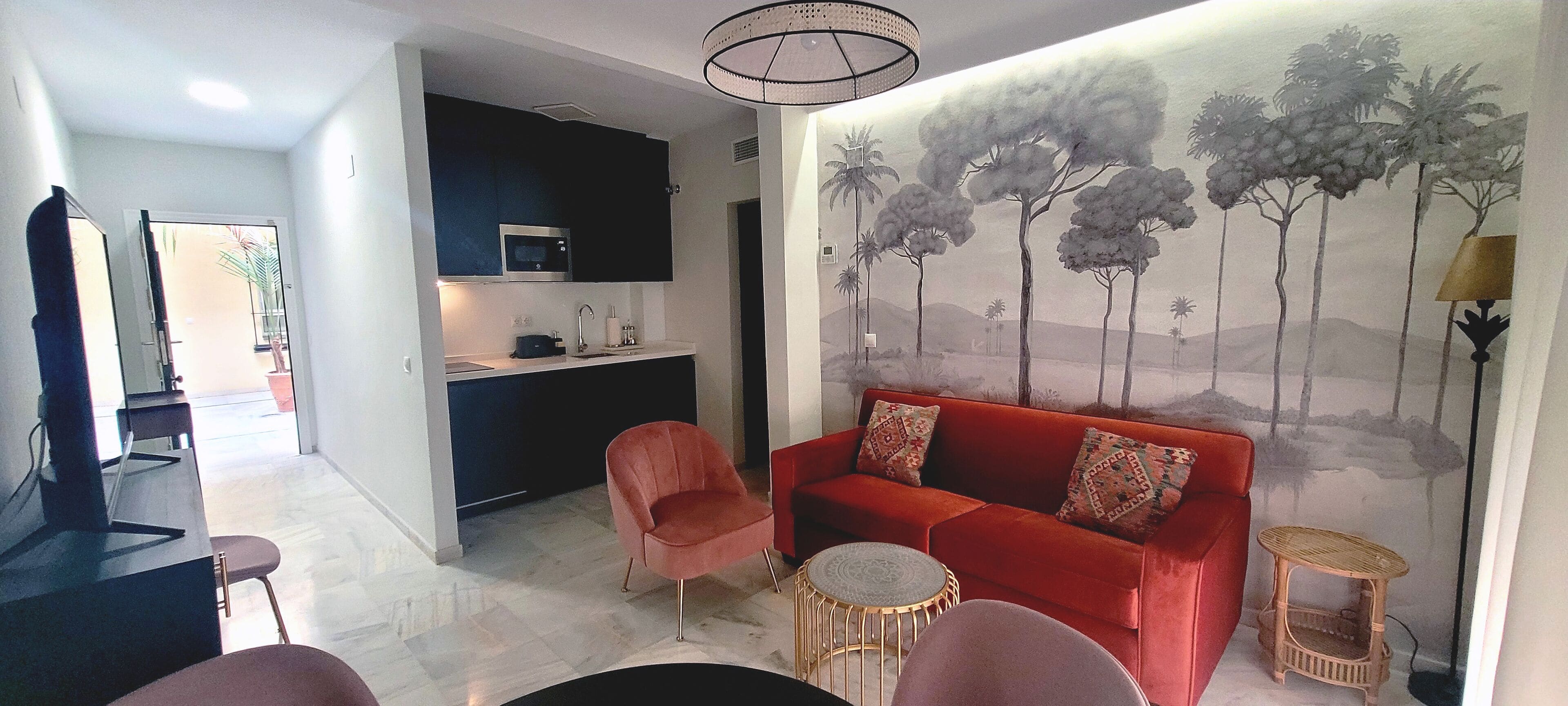 A modern living room with a red sofa, a small round table, and a wall mural of trees.