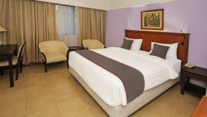 Ein Hotelzimmer mit einem großen Bett, zwei Stühlen, einem kleinen Tisch und einem Nachttisch.