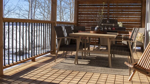 Een overdekt terras buiten met een houten tafel en stoelen, een barbecue en uitzicht op een besneeerd landschap.