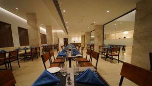 Un área de comedor con varias mesas preparadas para el servicio, que incluye una barra alargada y sillas dispuestas alrededor.
