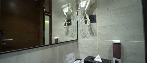 A bathroom with two hair dryers mounted on the wall, a tissue box, and a soap dispenser.