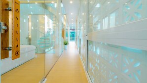 Un pasillo moderno de hotel con paredes de vidrio, una puerta de madera con la etiqueta 'VILLA' y una escalera al fondo.