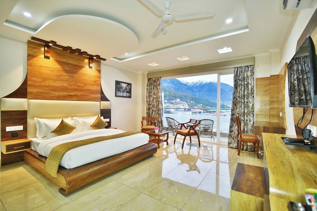 A modern hotel room with a large bed, a desk, and a balcony with a mountain view.