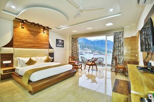 A modern hotel room with a large bed, a desk, and a balcony with a mountain view.