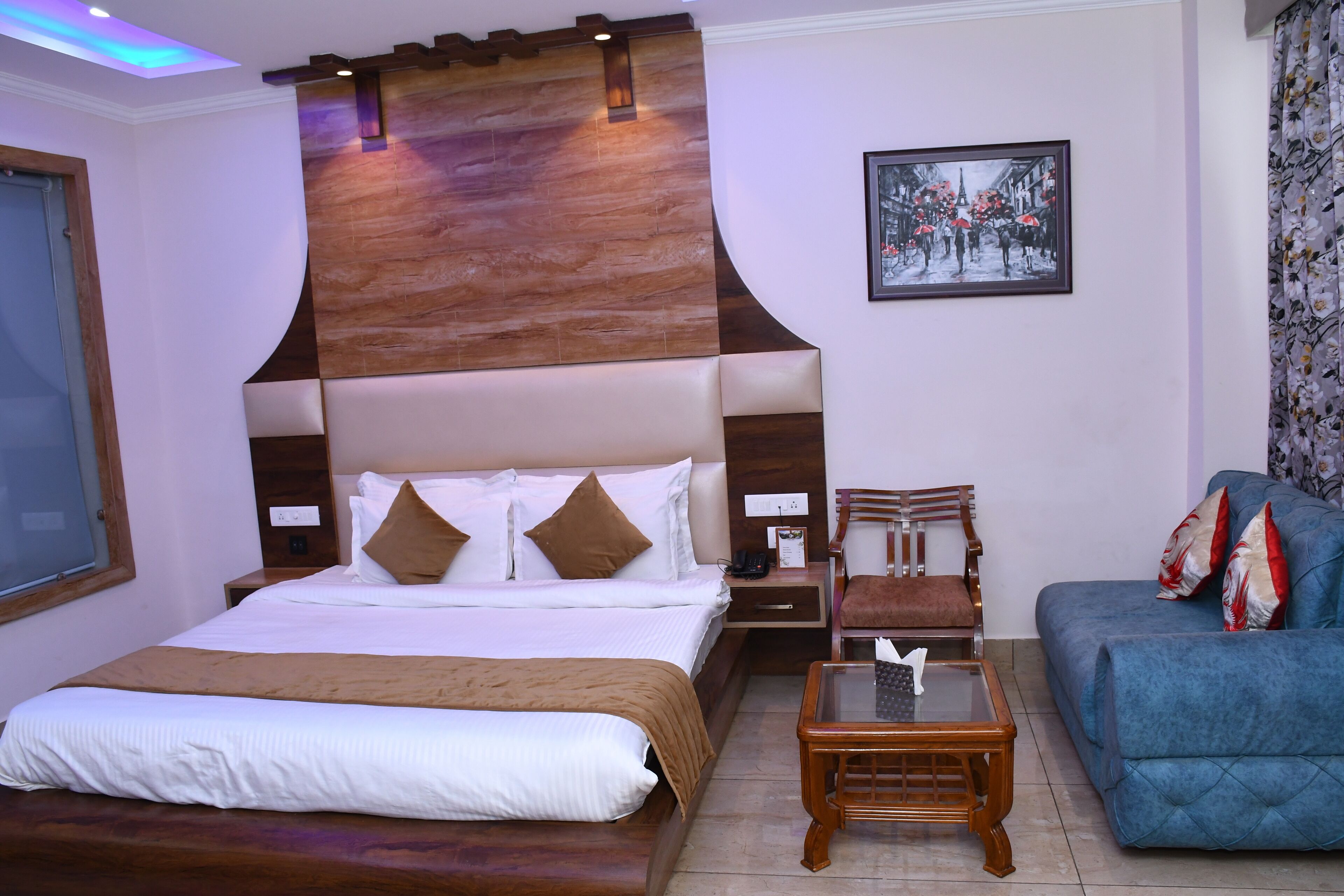 A hotel room with a large bed, a wooden headboard, a blue sofa, a small table, and a framed picture on the wall.