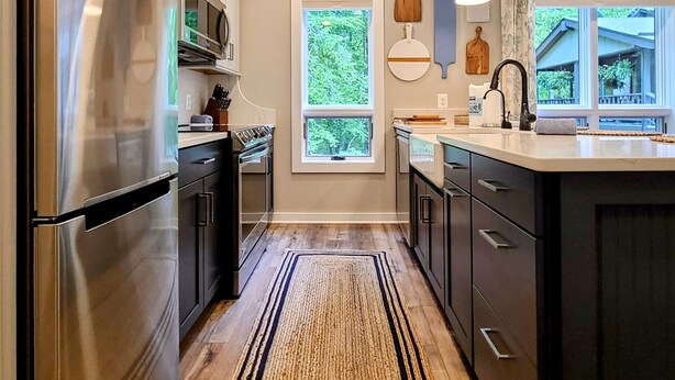 A modern kitchen with stainless steel appliances, a wooden floor, and a large window providing natural light. - Bear Mountain Cottage (Paeonian Springs)