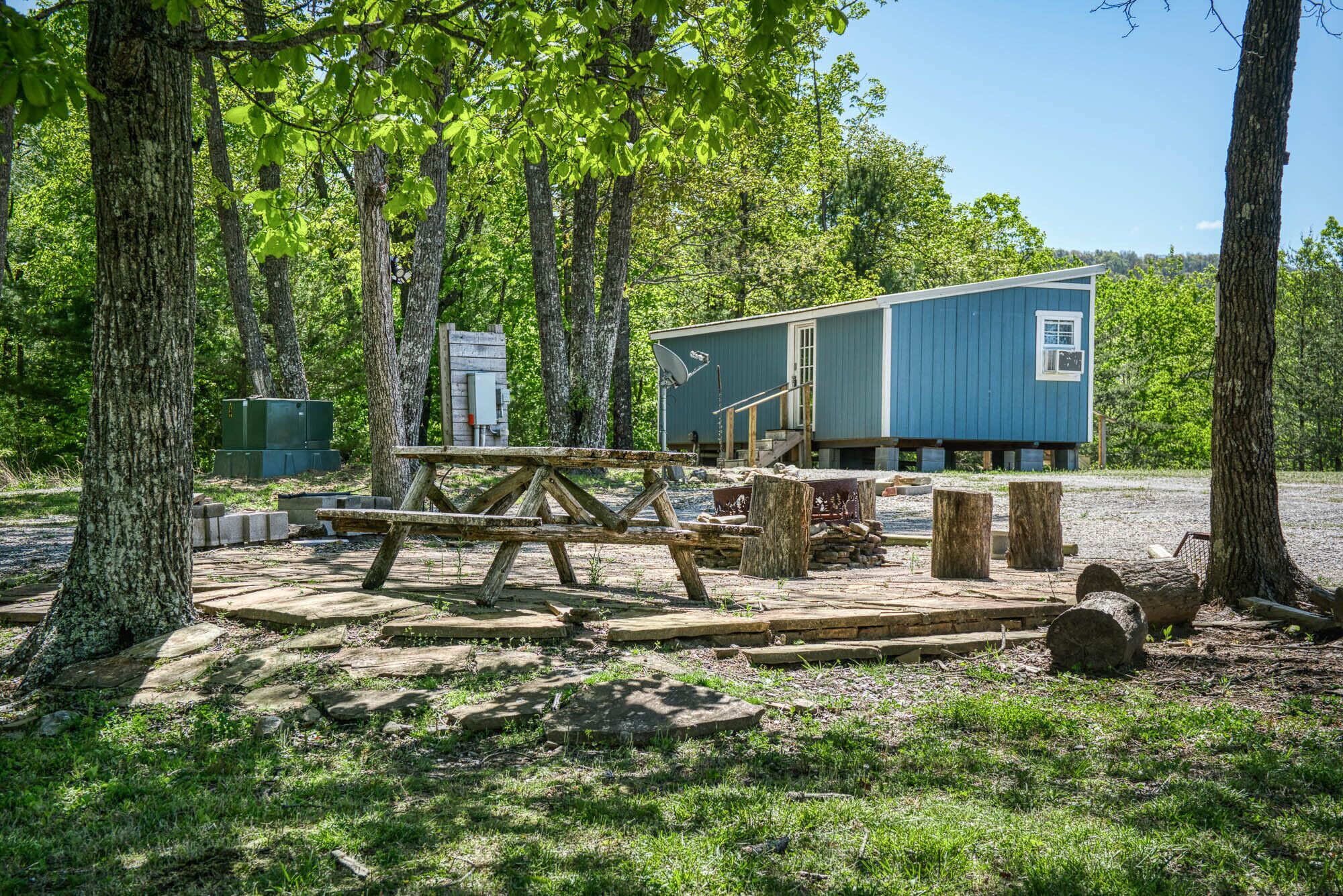 Un chalet rustique à l’extérieur bleu, entouré d’arbres et doté d’une terrasse en bois.