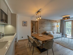 A modern kitchen with a dining area, wooden flooring, and a large window with curtains.