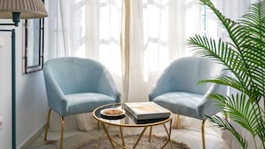 Quarto com duas poltronas azul-claras, uma mesinha redonda com um livro e uma tigela, uma luminária e uma planta grande.