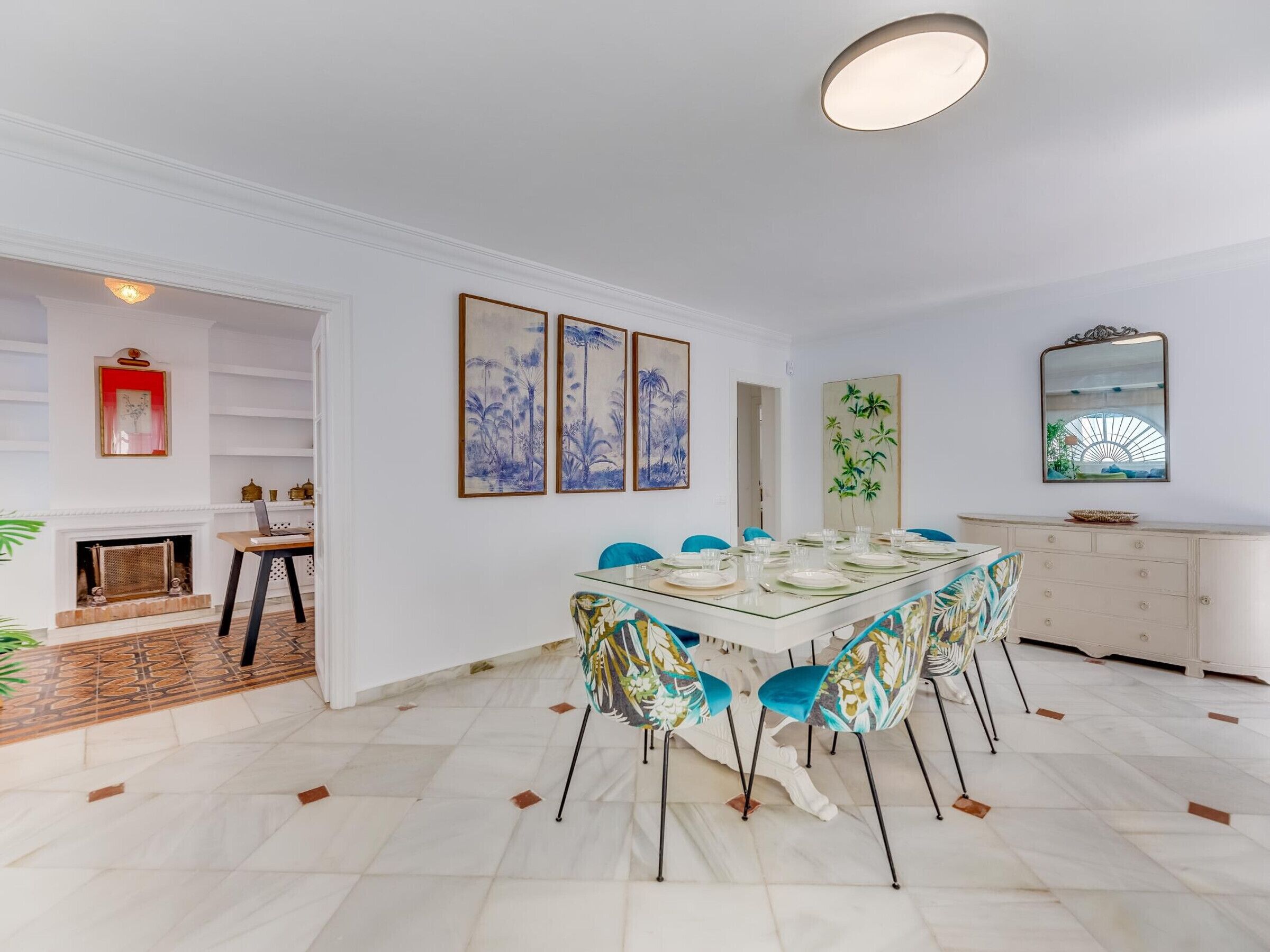 A dining area with a glass table, blue chairs, and a white cabinet.