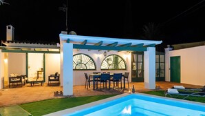 Área de piscina com pergolado, área de estar externa e mesa de jantar.