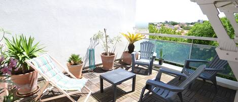 A balcony with wooden flooring, potted plants, and outdoor furniture including lounge chairs and a table.