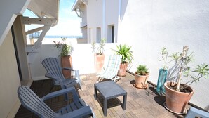 Un patio cubierto al aire libre con dos sillones, una mesita y varias plantas en macetas.