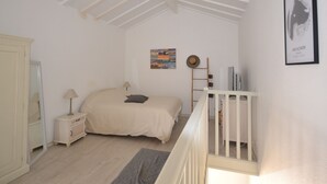 Un dormitorio con cama, mesita de noche, cómoda, escalera y un cuadro en la pared.
