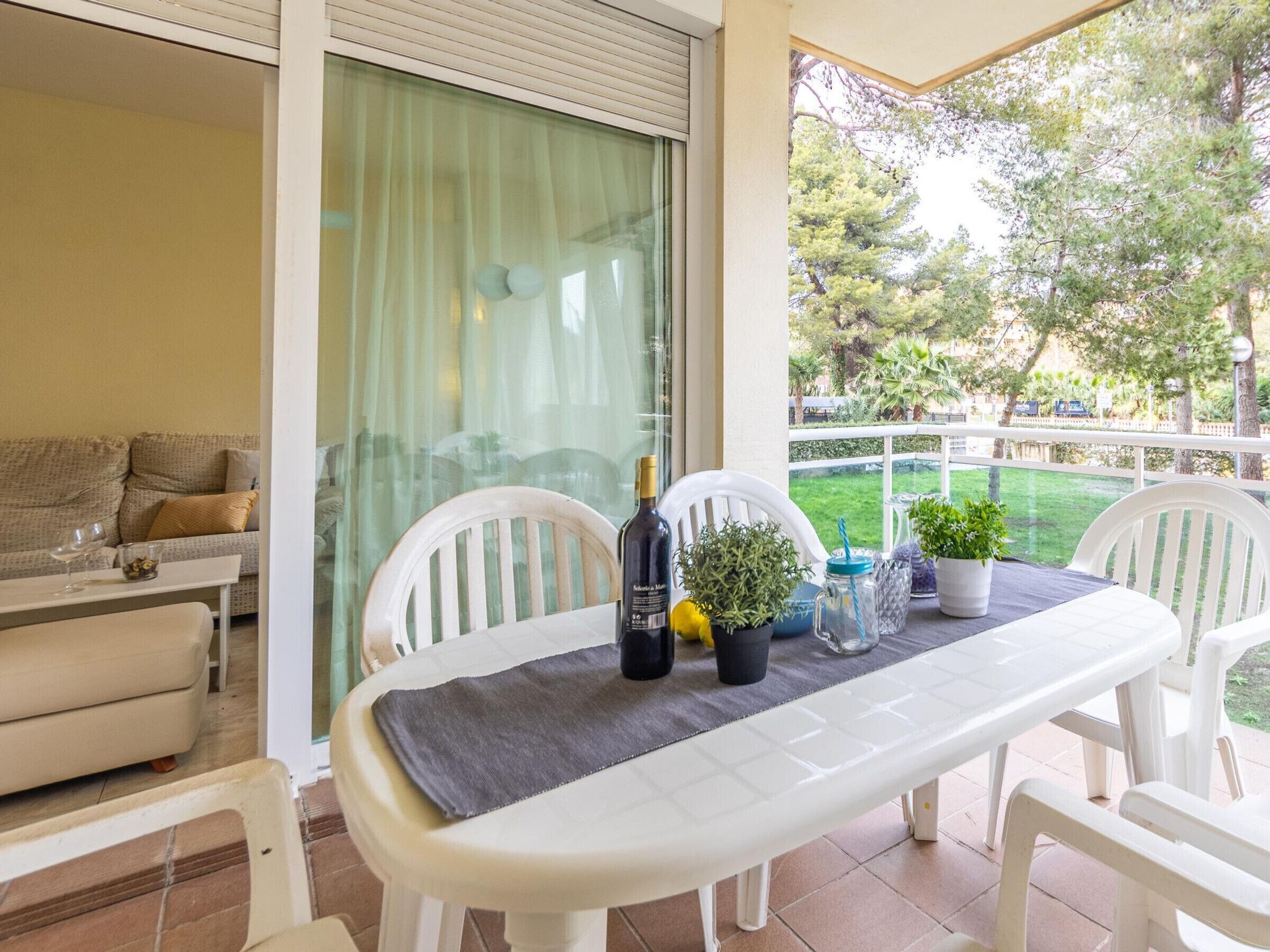 A patio with a table set for two, a bottle of wine, and potted plants.