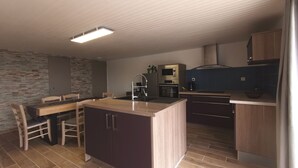 A compact kitchen with a central island, a dining area with chairs, and a stone accent wall. - Charming Farmhouse Retreat: Farm Life, Wildlife & Scenic Views, Perfect for Family Holidays (Autrac)