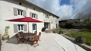 A patio with a table and chairs, a red umbrella, and a white building with windows and a door. - Charming Farmhouse Retreat: Farm Life, Wildlife & Scenic Views, Perfect for Family Holidays (Autrac)