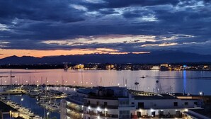 Ein Yachthafen mit vertäuten Booten, Gebäude mit Balkonen und einem ruhigen Wasserspiegel, der den Himmel widerspiegelt.