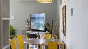 A dining area with a round table and four yellow chairs, a hanging light fixture, and a television on a stand in the background. - Sunshine Paradise: Oceanfront Retreat Awaits (North Topsail Beach)
