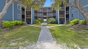 A multi-story apartment building with a central courtyard, a paved walkway, and a picnic table. - Sunshine Paradise: Oceanfront Retreat Awaits (North Topsail Beach)