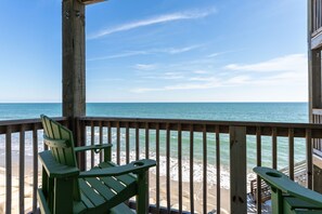 Una terraza de madera con dos sillones Adirondack verdes frente a una playa con vistas al océano.