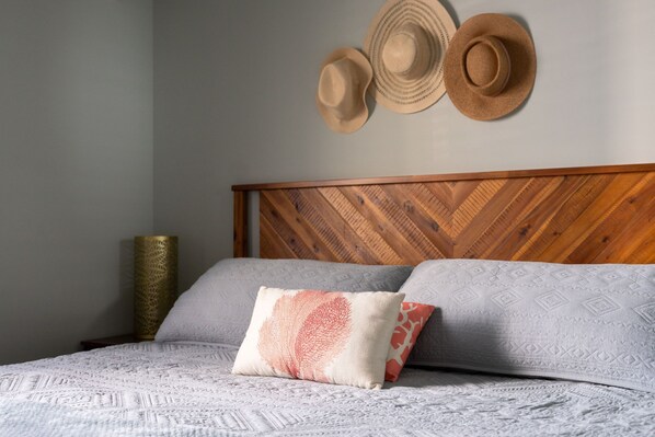 Una cama bien hecha con ropa de cama estampada, cabecera de madera y sombreros decorativos en la pared.
