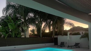 Un espace piscine extérieur moderne, doté d’une piscine aux bords incurvés, entouré d’un petit muret et agrémenté d’une végétation tropicale luxuriante.