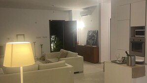 Un salon moderne comprenant un canapé, une lampe et un coin cuisine équipé d’appareils électroménagers.