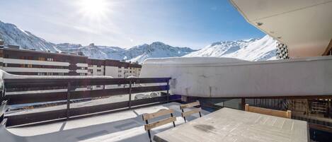 A snow-covered outdoor seating area with a table and chairs, overlooking a mountainous landscape.