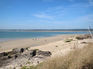 A beach with clear skies, rocky foreground, and calm sea.
