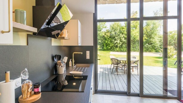 Une cuisine moderne dotée d’un four encastré, d’un évier et d’une fenêtre donnant sur une terrasse aménagée avec du mobilier d’extérieur.