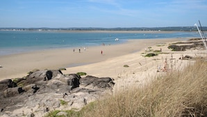 Une plage avec un ciel dégagé, un premier plan rocheux et une mer calme.