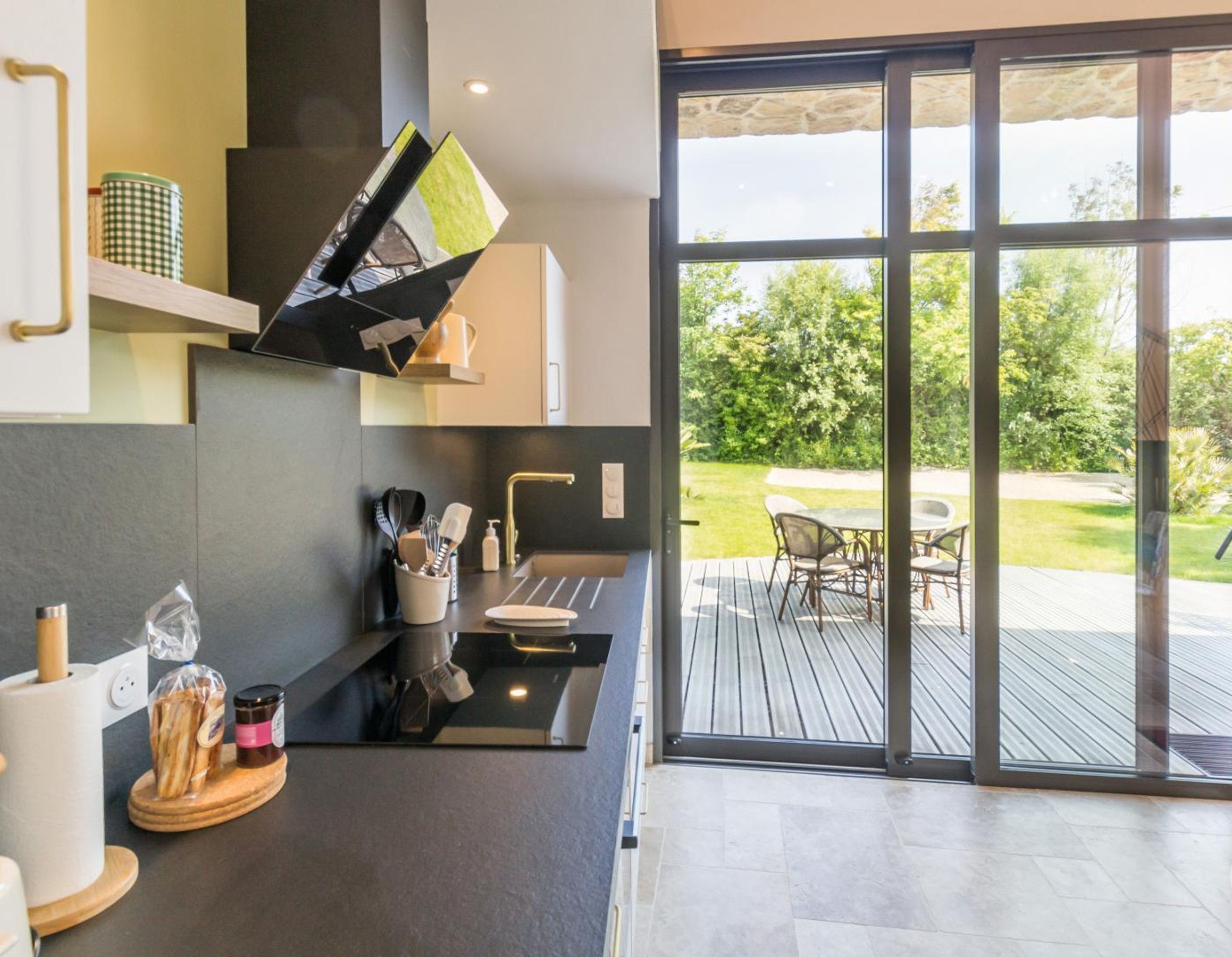 Una cocina moderna con horno empotrado, un lavamanos y una ventana con vista a una terraza amueblada.
