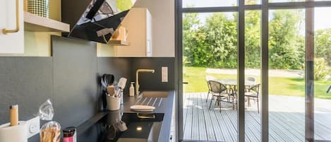 A modern kitchen with a built-in oven, a sink, and a window overlooking a deck with outdoor furniture.