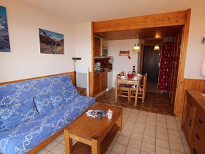 Une pièce chaleureuse avec un canapé bleu à motifs, une table à manger en bois avec des chaises, un petit coin cuisine et un plafond en bois.