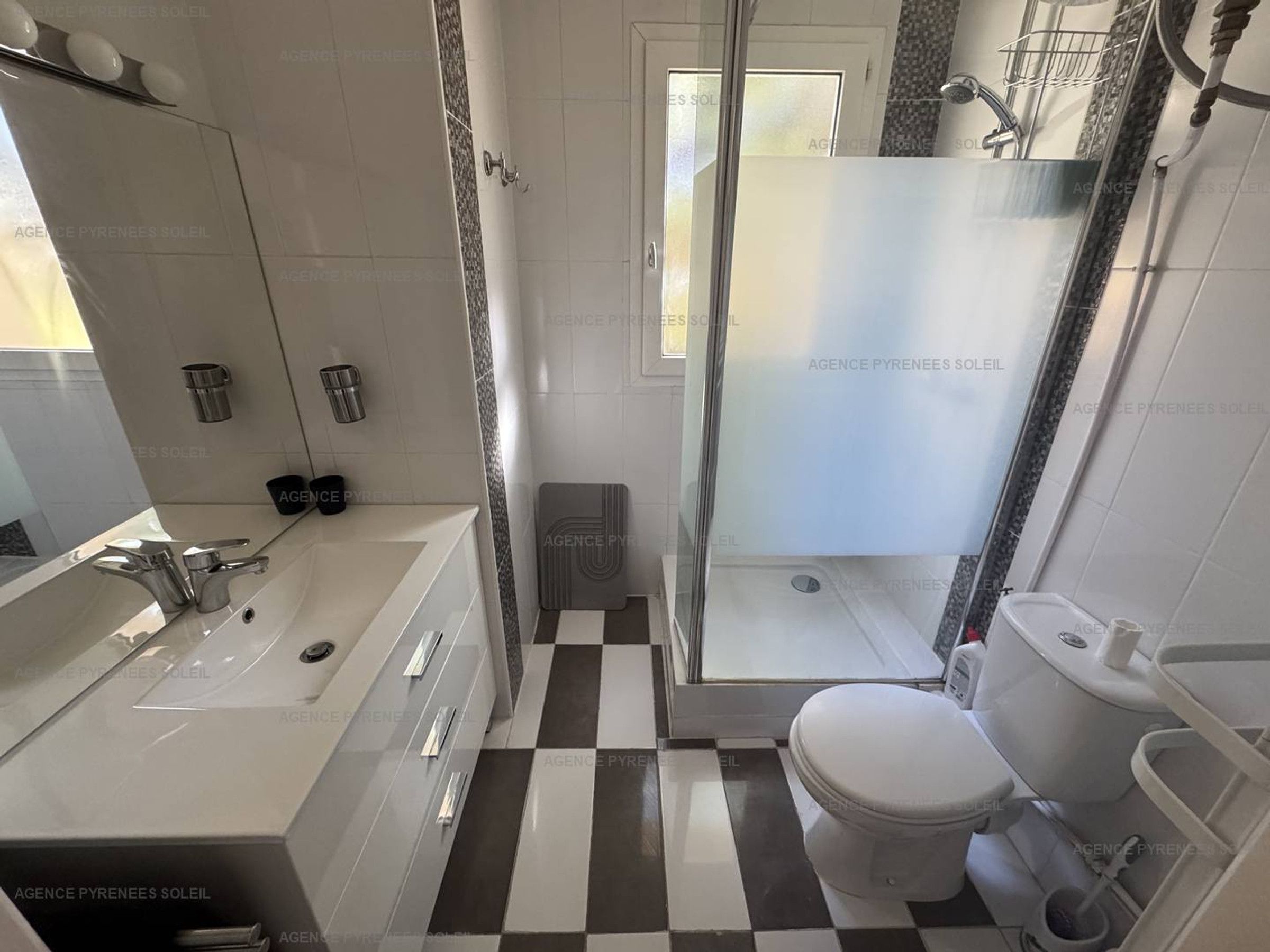 Un baño con piso a cuadros, inodoro blanco, lavamanos con espejo y zona de ducha.