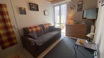Un salon confortable avec un canapé, une petite table sur laquelle se trouve une lampe, et un téléviseur fixé au mur.
