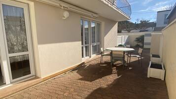 Une terrasse avec une table et des chaises, une porte-fenêtre coulissante et un petit balcon.