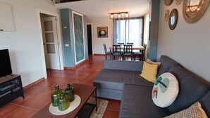 Un salon avec un canapé gris, une table basse et un meuble pour la télévision. Il y a également un coin repas avec une table et des chaises.