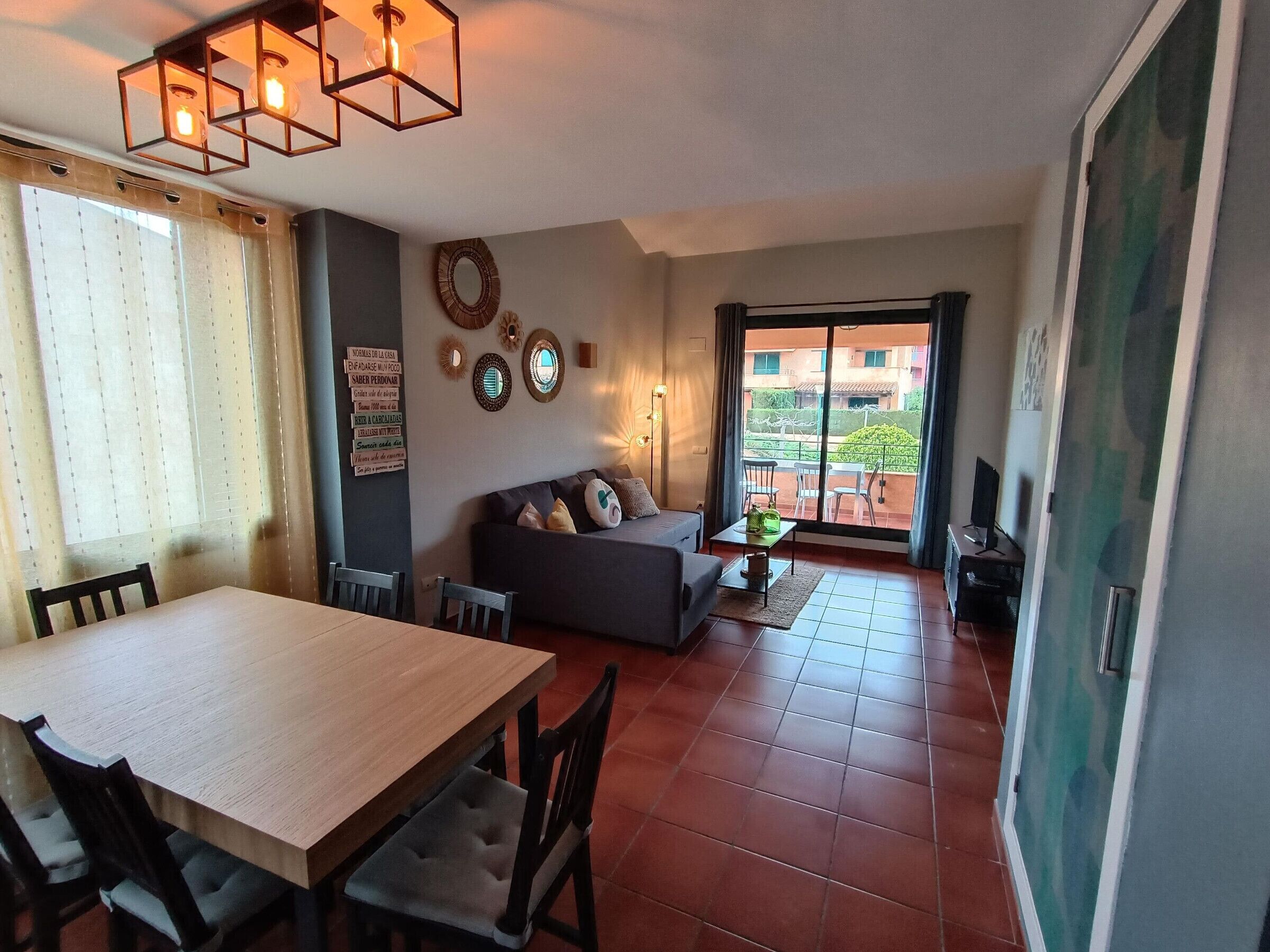 A living room with a sofa, a dining table with chairs, and a balcony with a view of buildings.